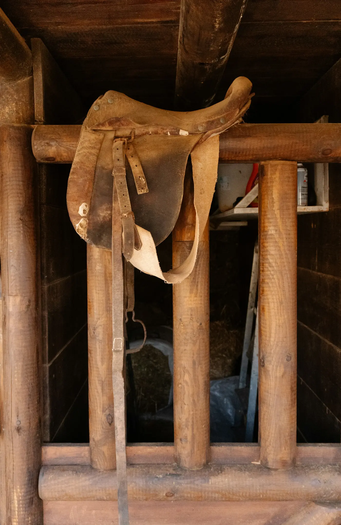 Ein abgenutzter Ledersattel liegt auf einem Holzbalken im Stall